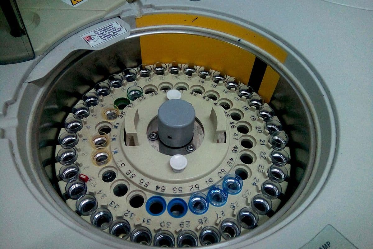 Carrossel circular numerado com dezenas de copinhos de amostra dentro de um analisador automático de laboratório