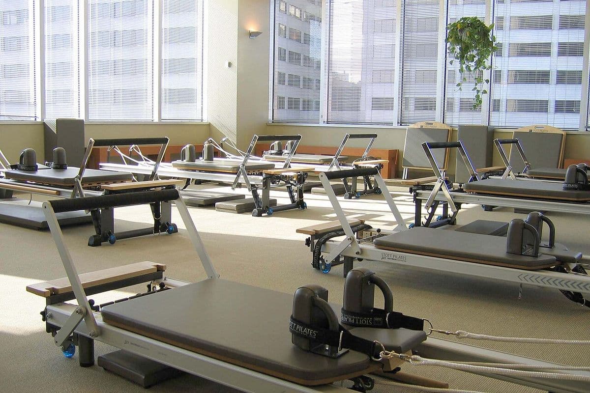 Sala de studio com vários aparelhos reformer de pilates enfileirados diante de janelas