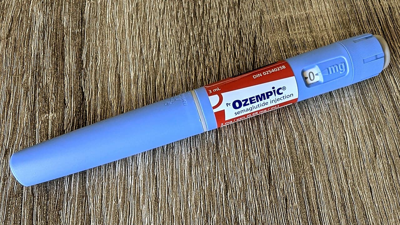 Caneta injetável azul de semaglutida, com rótulo vermelho e branco, sobre uma mesa de madeira