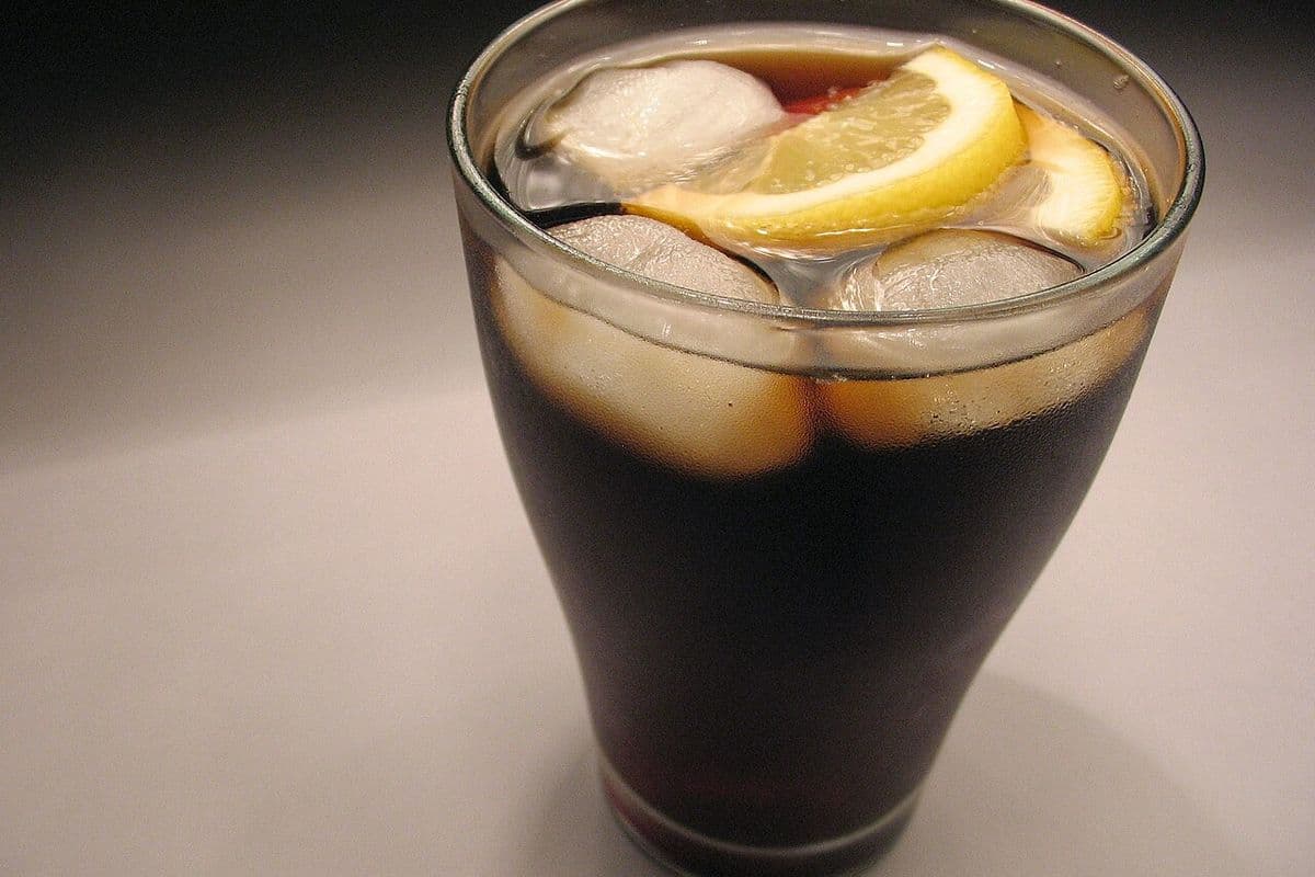 Copo de vidro com refrigerante de cola, cubos de gelo e duas fatias de limão sobre fundo cinza