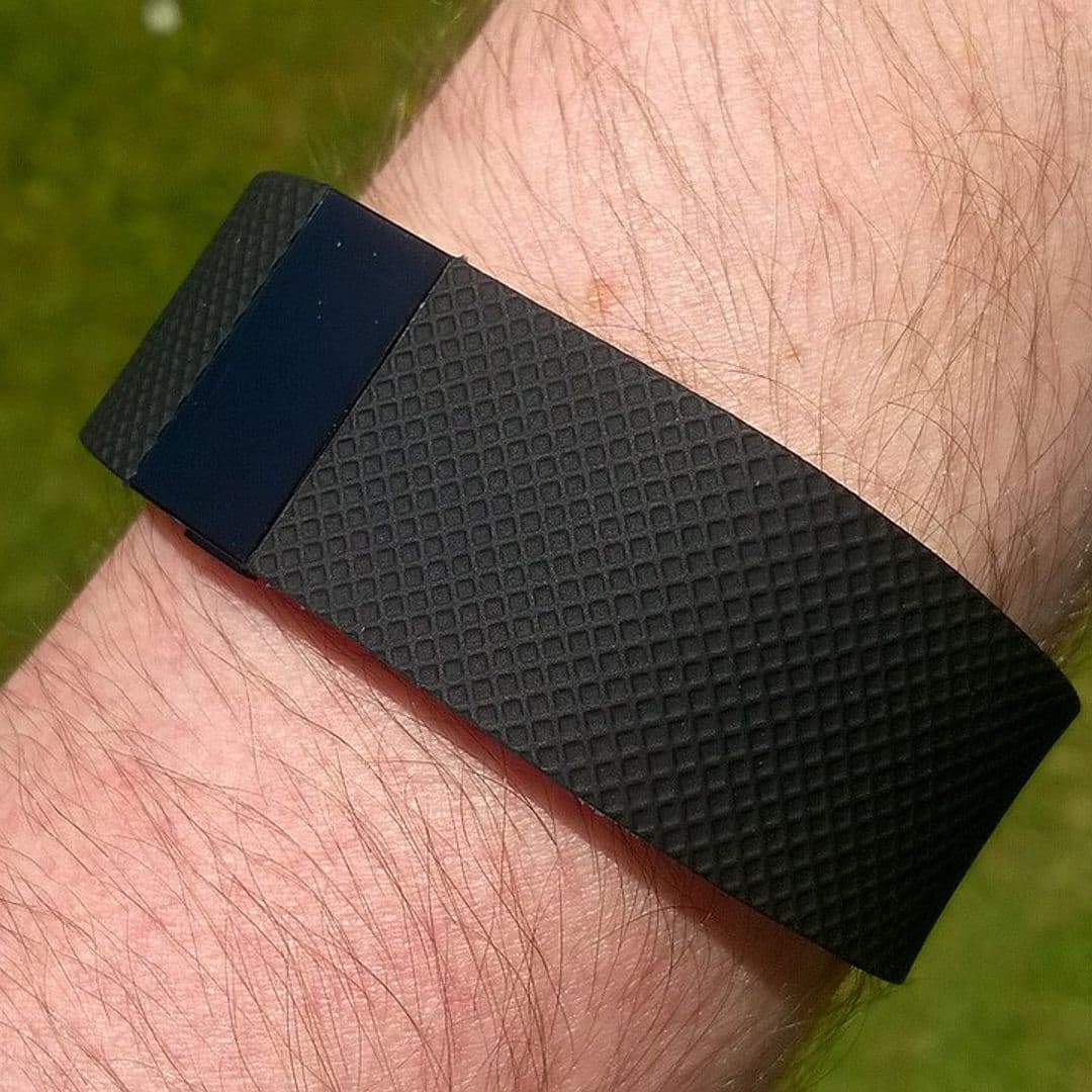 Pulseira Fitbit Charge HR preta presa ao pulso, com gramado ao fundo