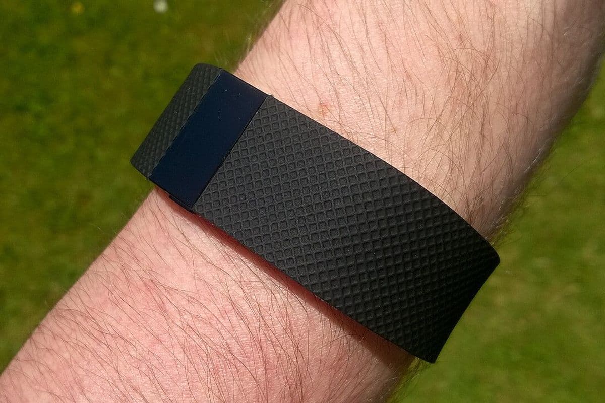 Pulseira Fitbit Charge HR preta presa ao pulso, com gramado ao fundo