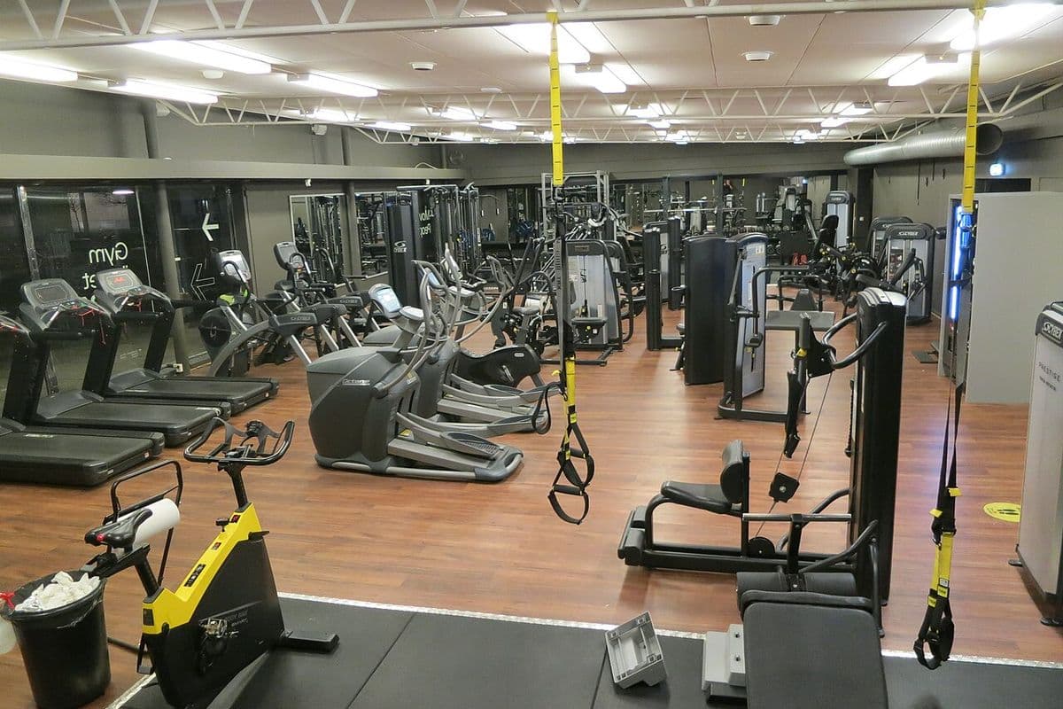 Salão de academia vazio com esteiras, elípticos, aparelhos de musculação e fitas de suspensão