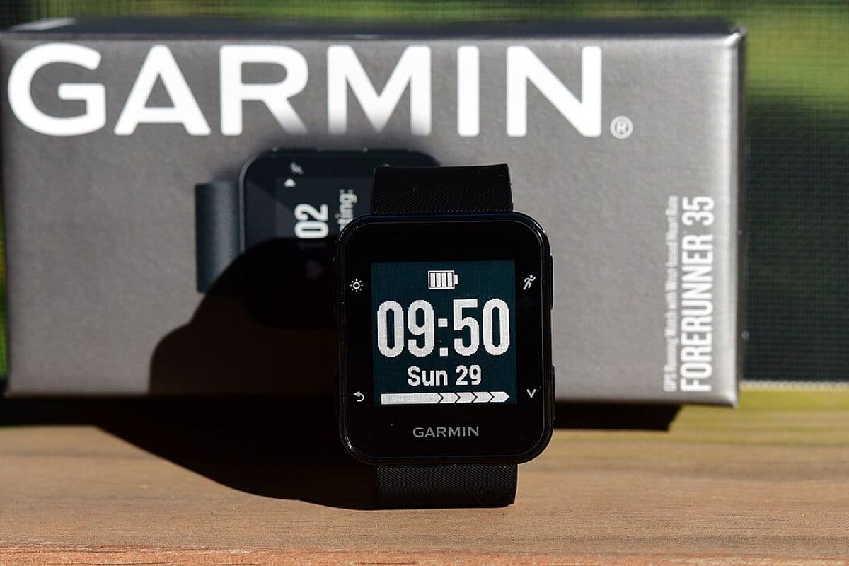 Relógio esportivo Garmin Forerunner 35 com a tela acesa, em frente à caixa do produto