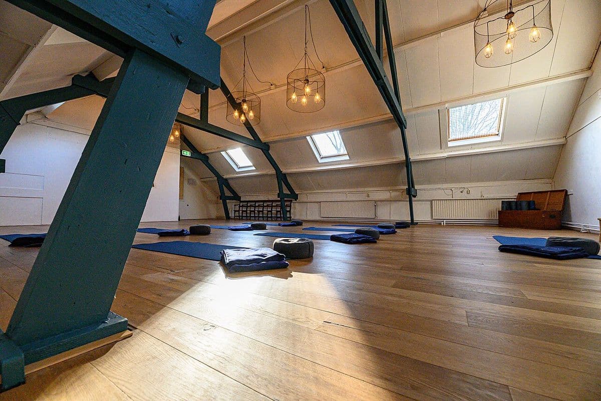 Sala de yoga vazia em sótão com piso de madeira, tapetes azuis, almofadas e luminárias pendentes