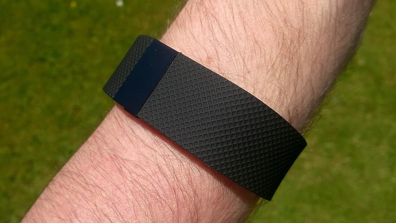 Pulseira Fitbit Charge HR preta presa ao pulso, com gramado ao fundo