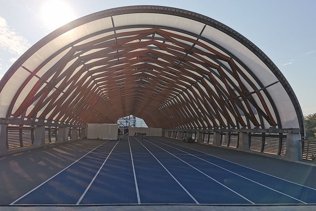 Pista de corrida azul de seis raias sob uma estrutura em arco de madeira e cobertura translúcida, sem pessoas