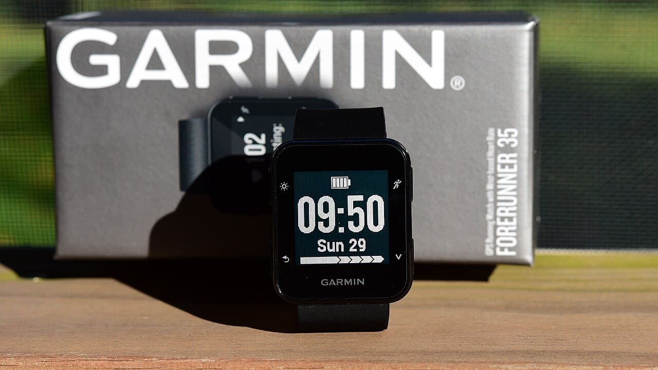 Relógio esportivo Garmin Forerunner 35 com a tela acesa, em frente à caixa do produto