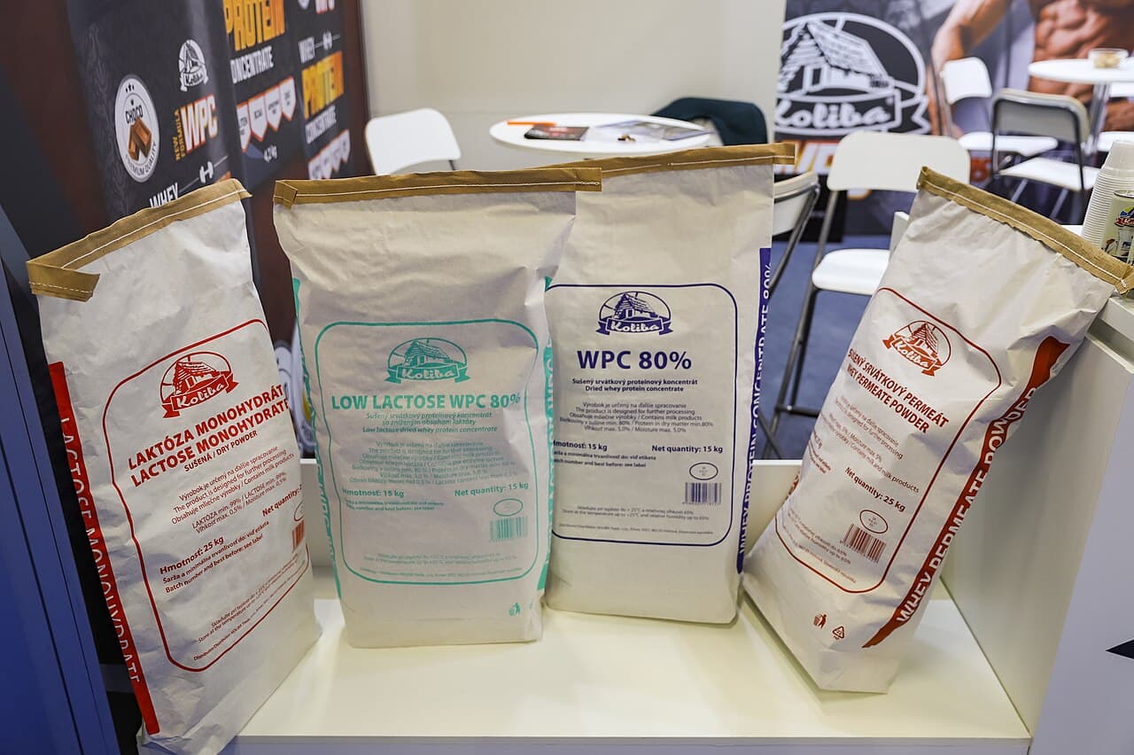 Quatro sacos de papel com lactose, concentrado de proteína do soro de leite WPC 80% e permeado de soro sobre um balcão de estande