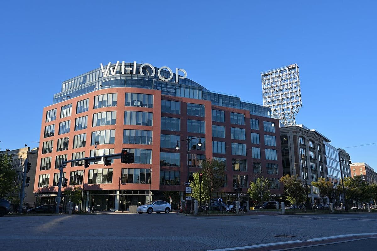 Prédio de tijolos e vidro com o letreiro Whoop no topo, numa esquina de Boston, sob céu azul