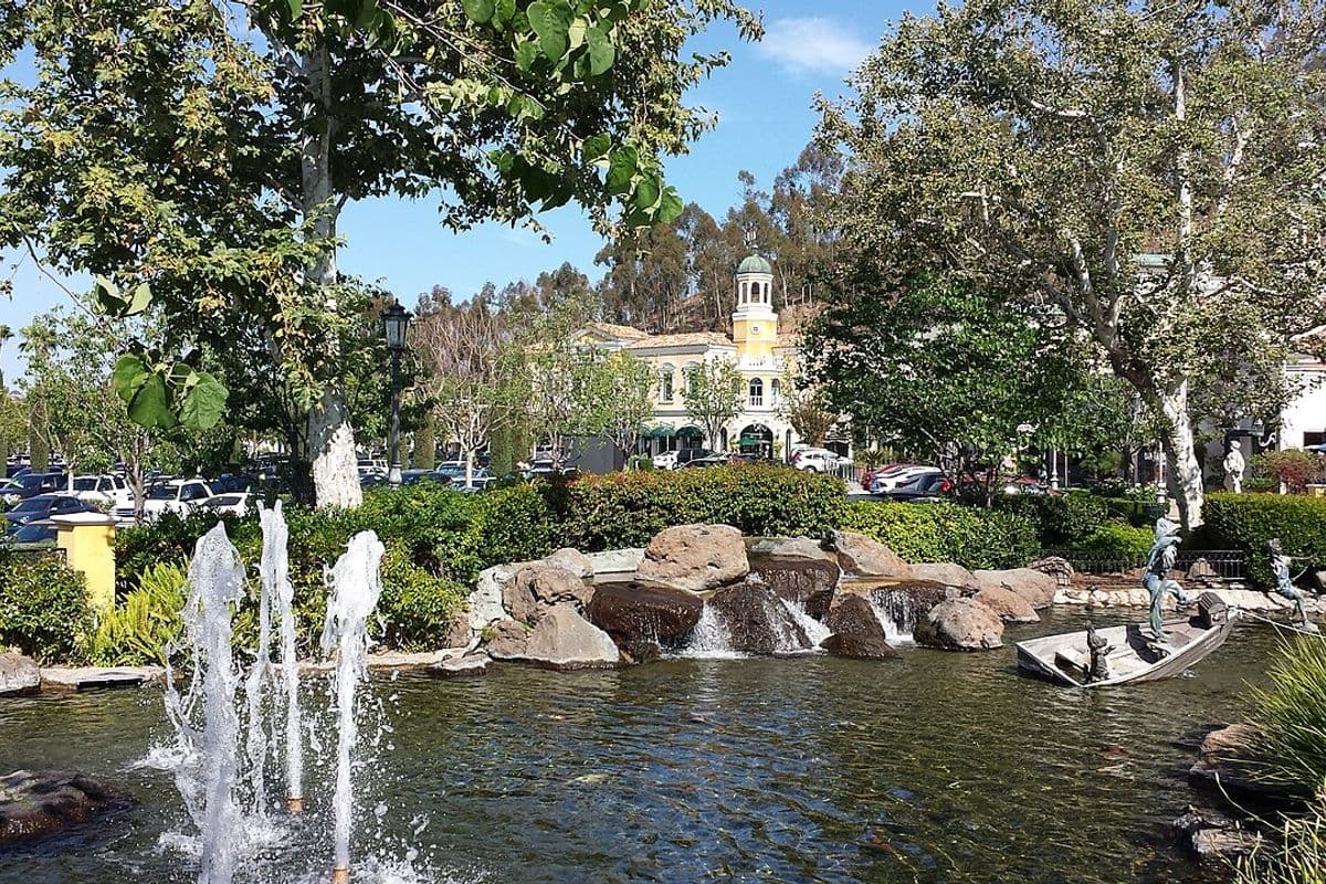 Fonte e lago com pedras no centro comercial a céu aberto The Commons at Calabasas, com um prédio de torre amarela ao fundo