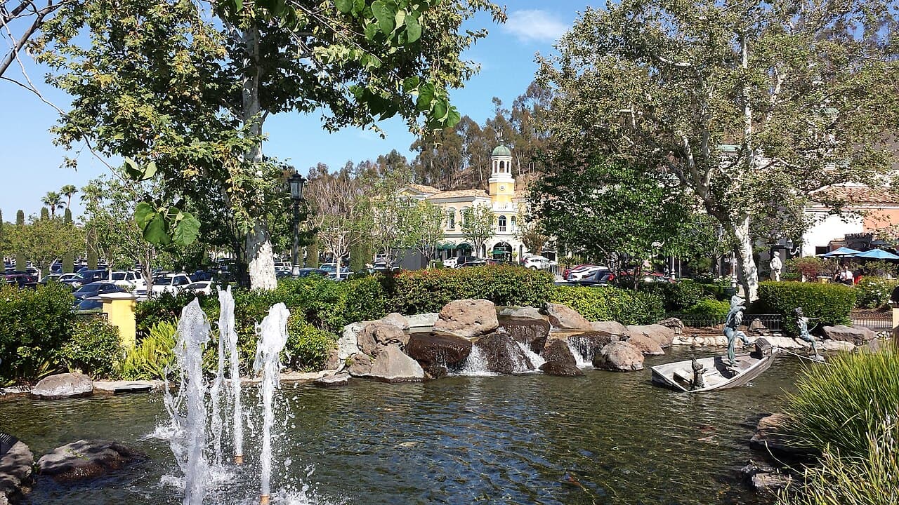 Fonte e lago com pedras no centro comercial a céu aberto The Commons at Calabasas, com um prédio de torre amarela ao fundo
